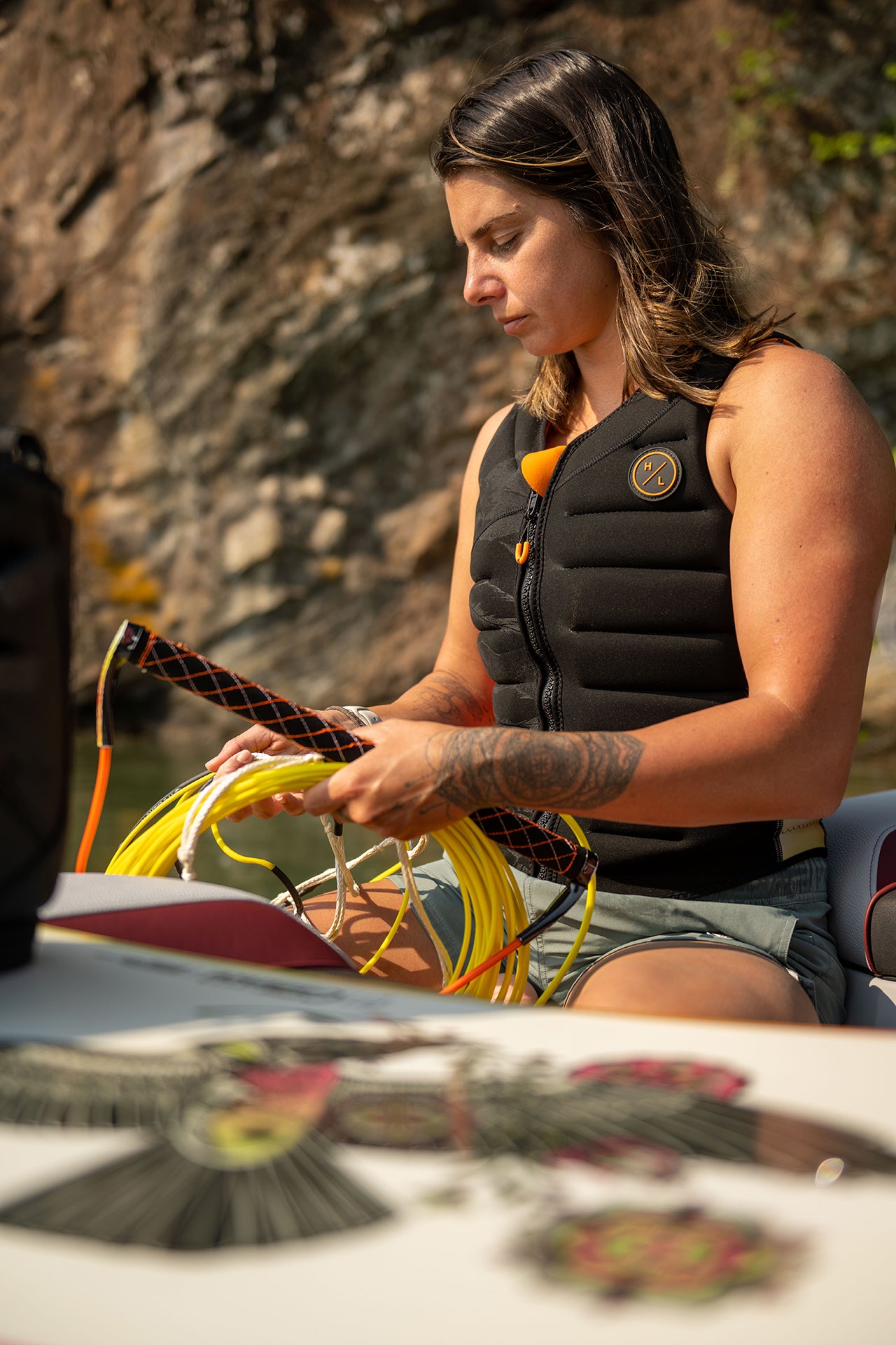 Person in a life vest handles wires or ropes outdoors, near a rocky background.