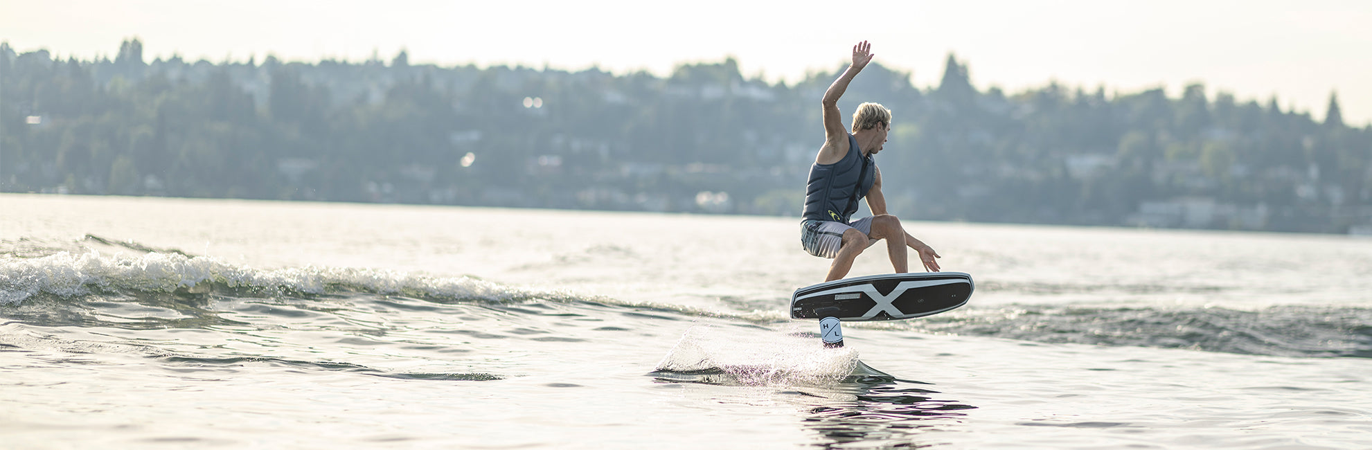 Person wakeboarding on a lake, performing a jump with a city in the background.