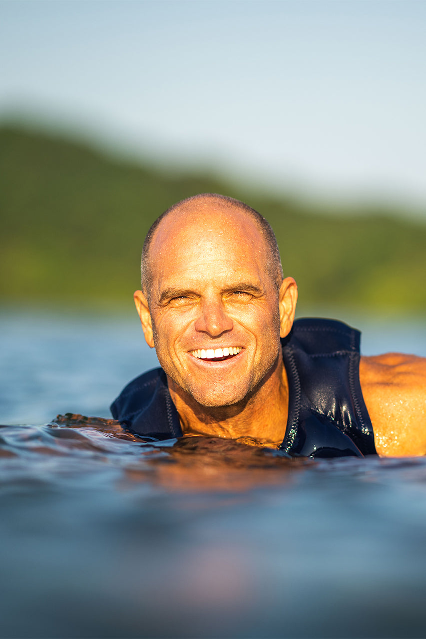 Smiling man in a life vest swimming in a lake, with a blurry green background.