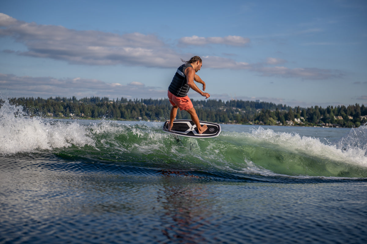 Person wakesurfing on a lake under a partly cloudy sky.