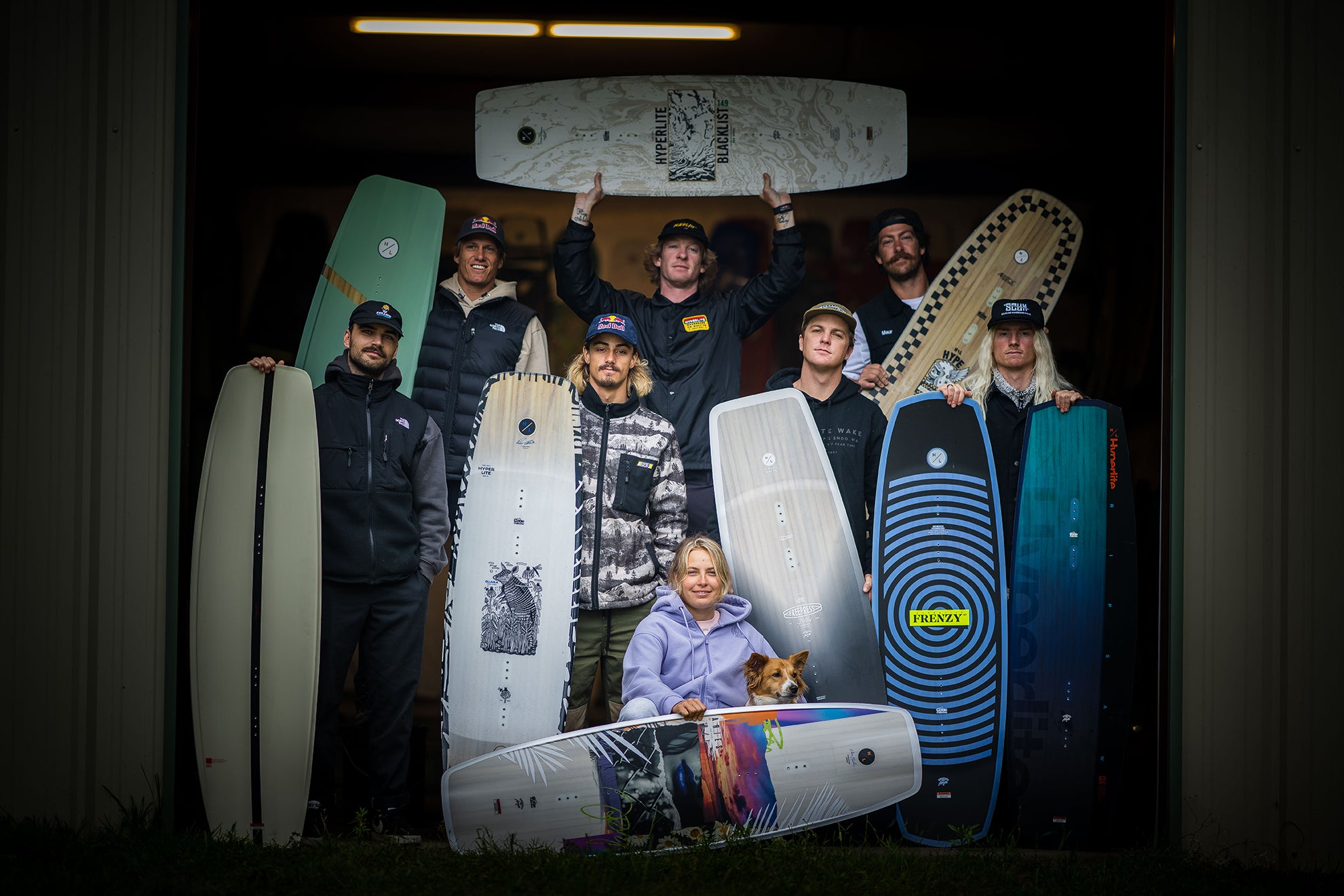 Group holding wakeboards indoors, with one person and a dog in front.