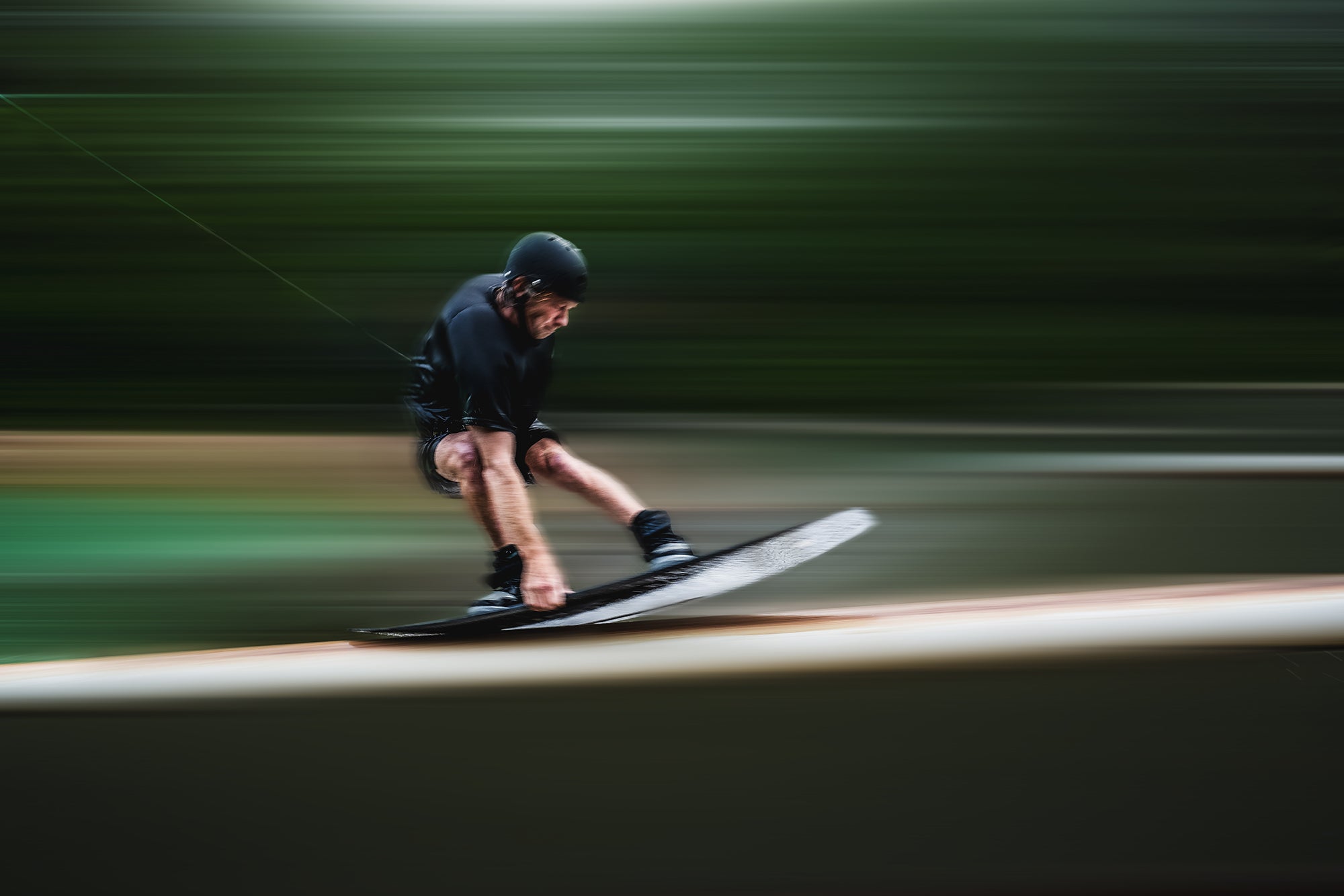 Person wakeboarding fast, wearing a helmet, with motion blur.