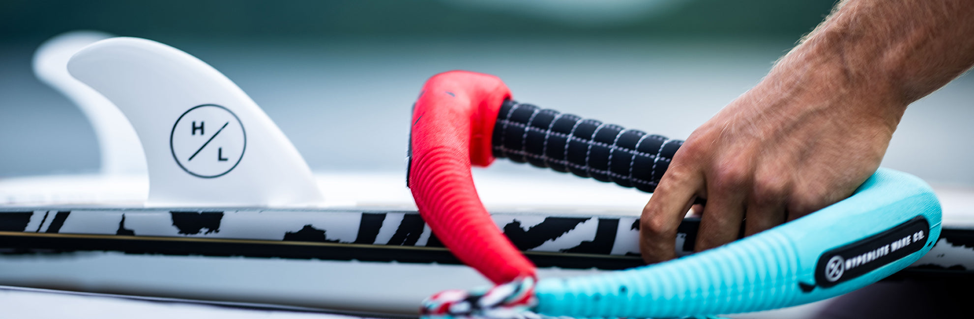 Close-up of a hand holding colorful water sports gear on a board with a fin, against a blurred background.