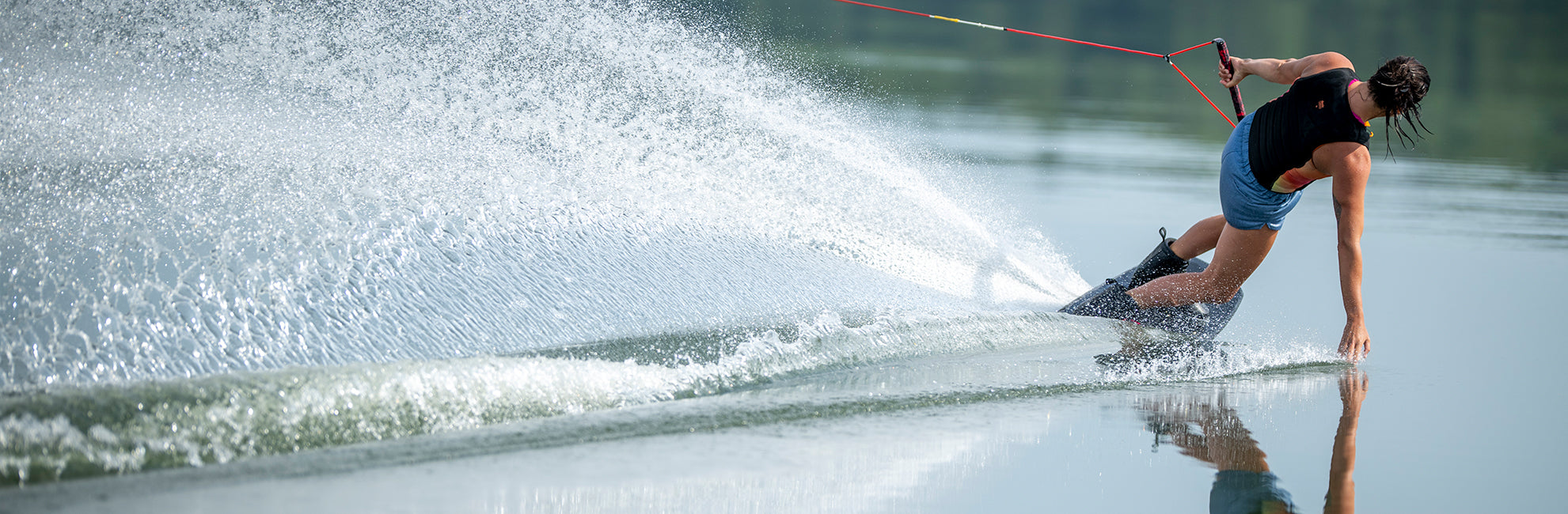 Person water skiing on a calm lake, creating a spray while holding a tow rope.