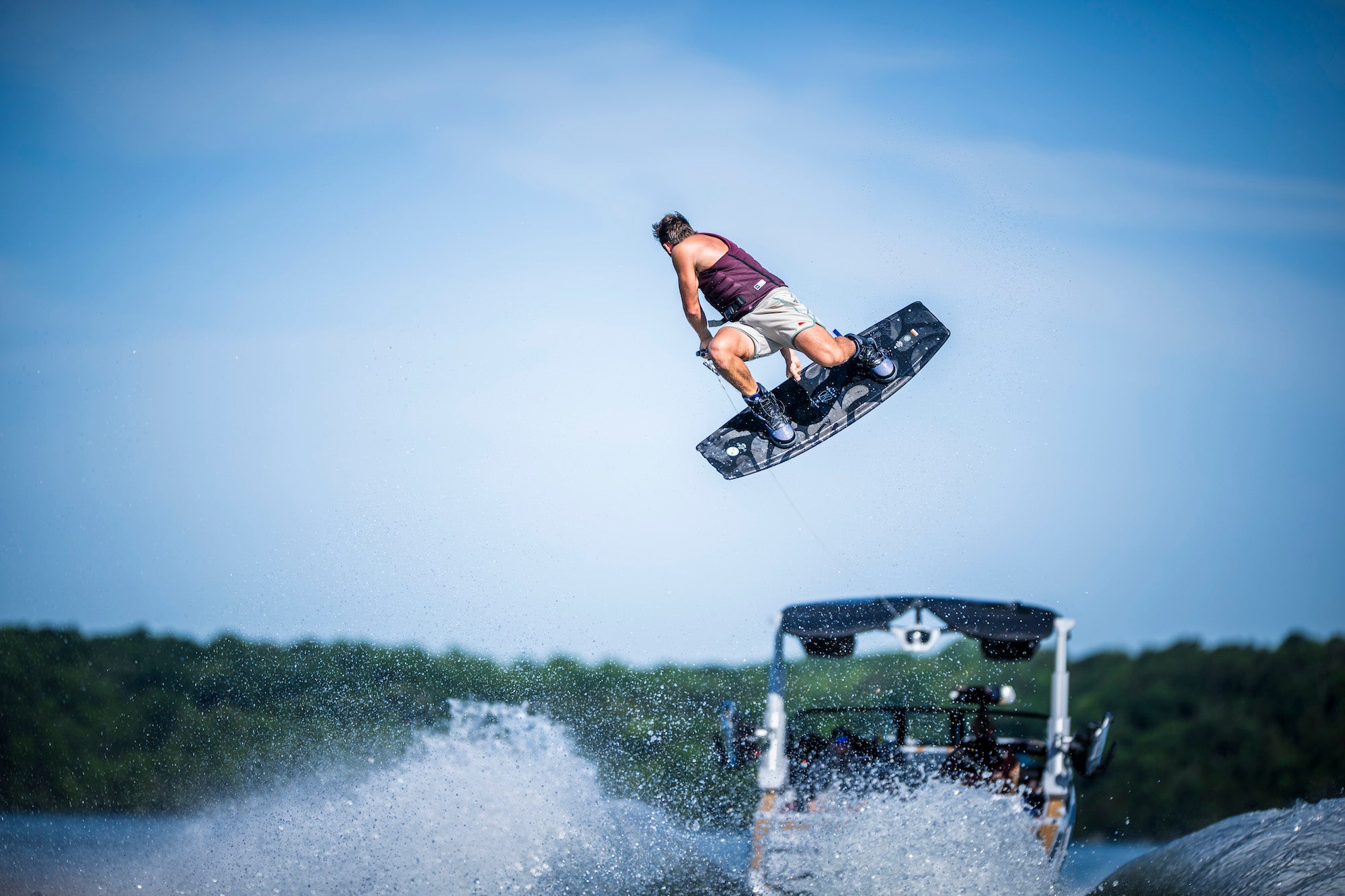 Person wakeboarding in mid-air behind a boat on a sunny day.