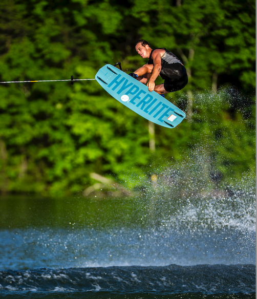 A person wakeboarding midair over water with a forest in the background.