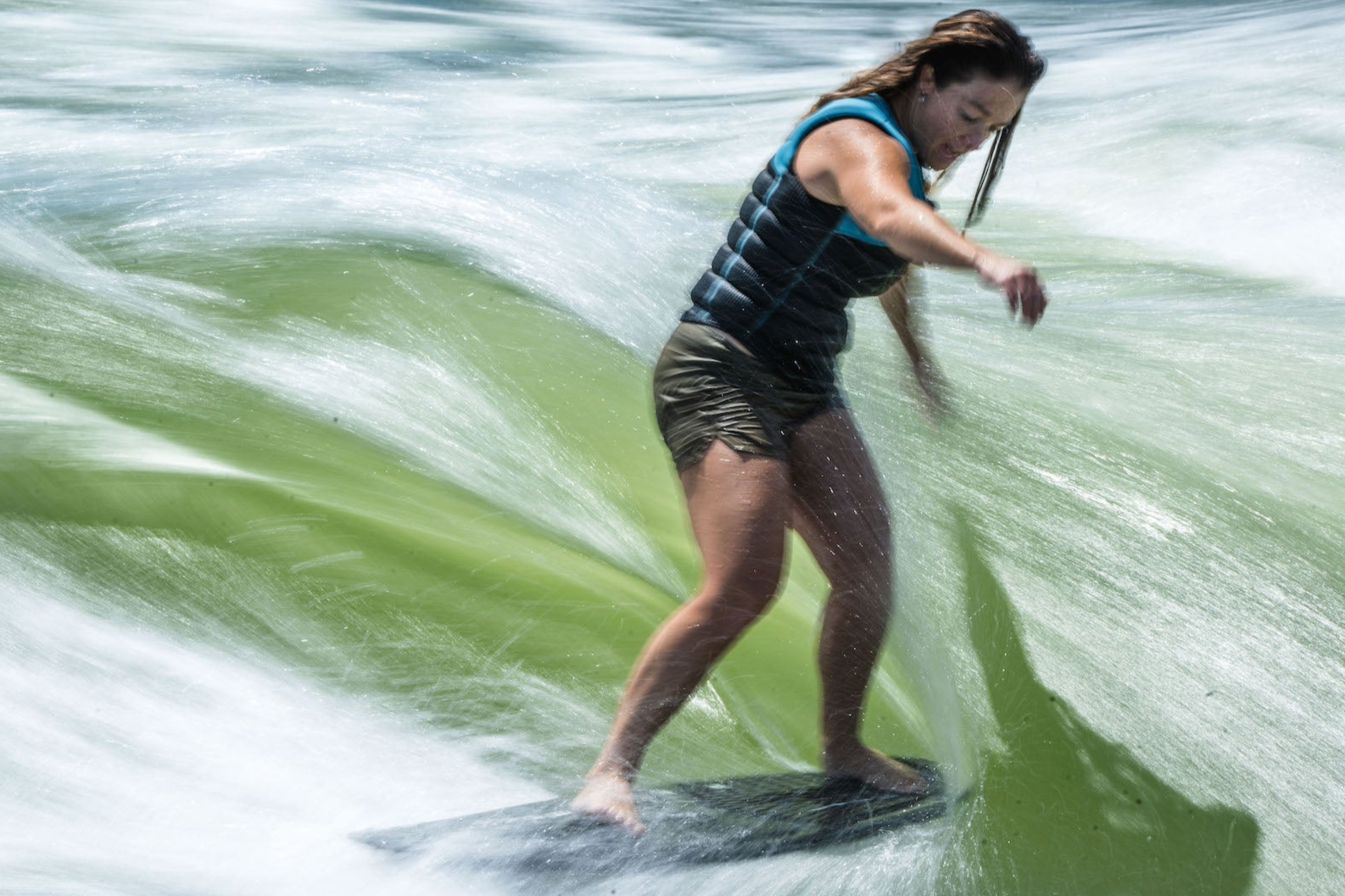 Person surfing on a wave, wearing a life vest and concentrating on balance.